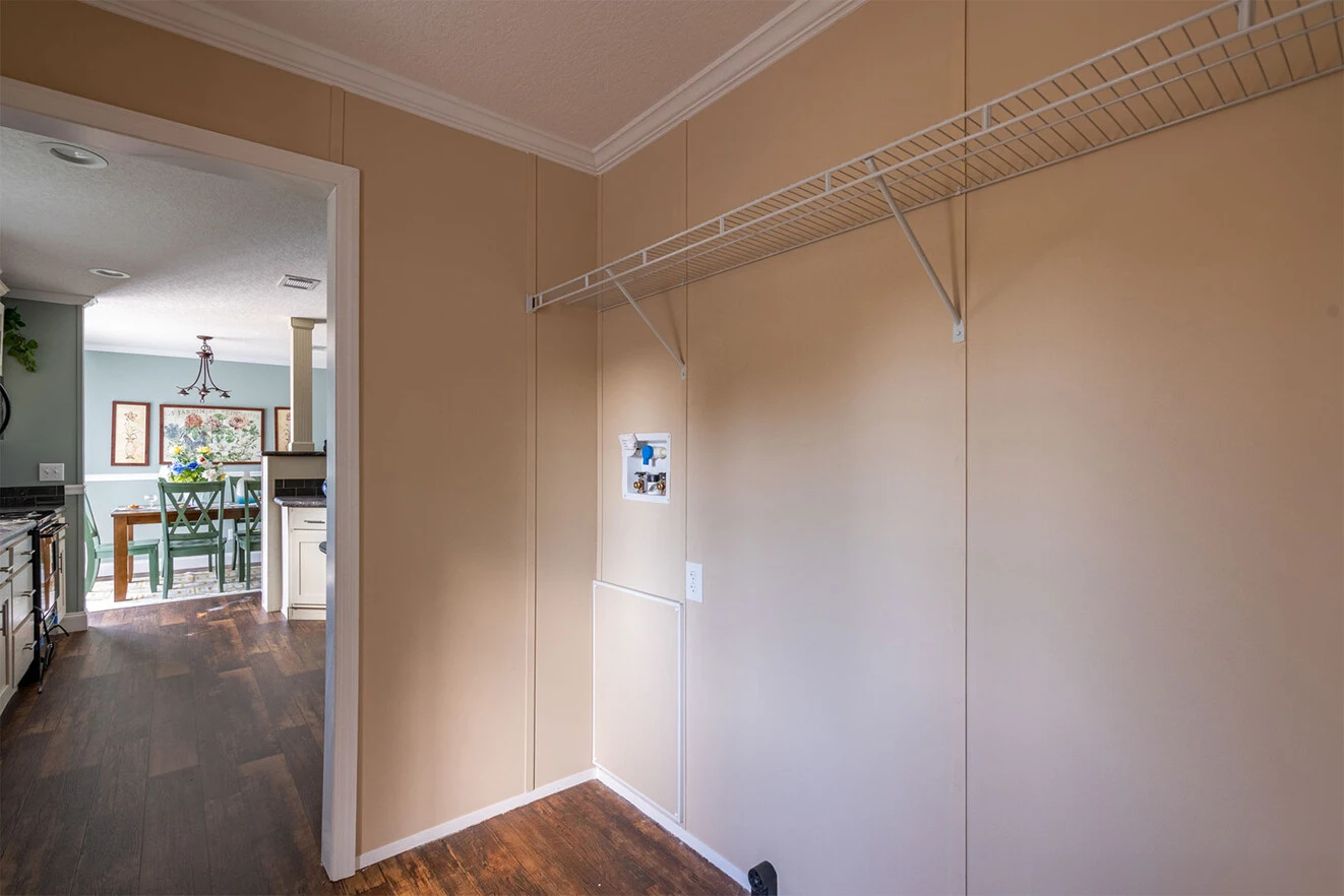te28523c_16_1713813628826_1323_12 Empty beige utility room with vinyl flooring, wire shelf on the wall, and an open doorway leading to a kitchen and dining area.