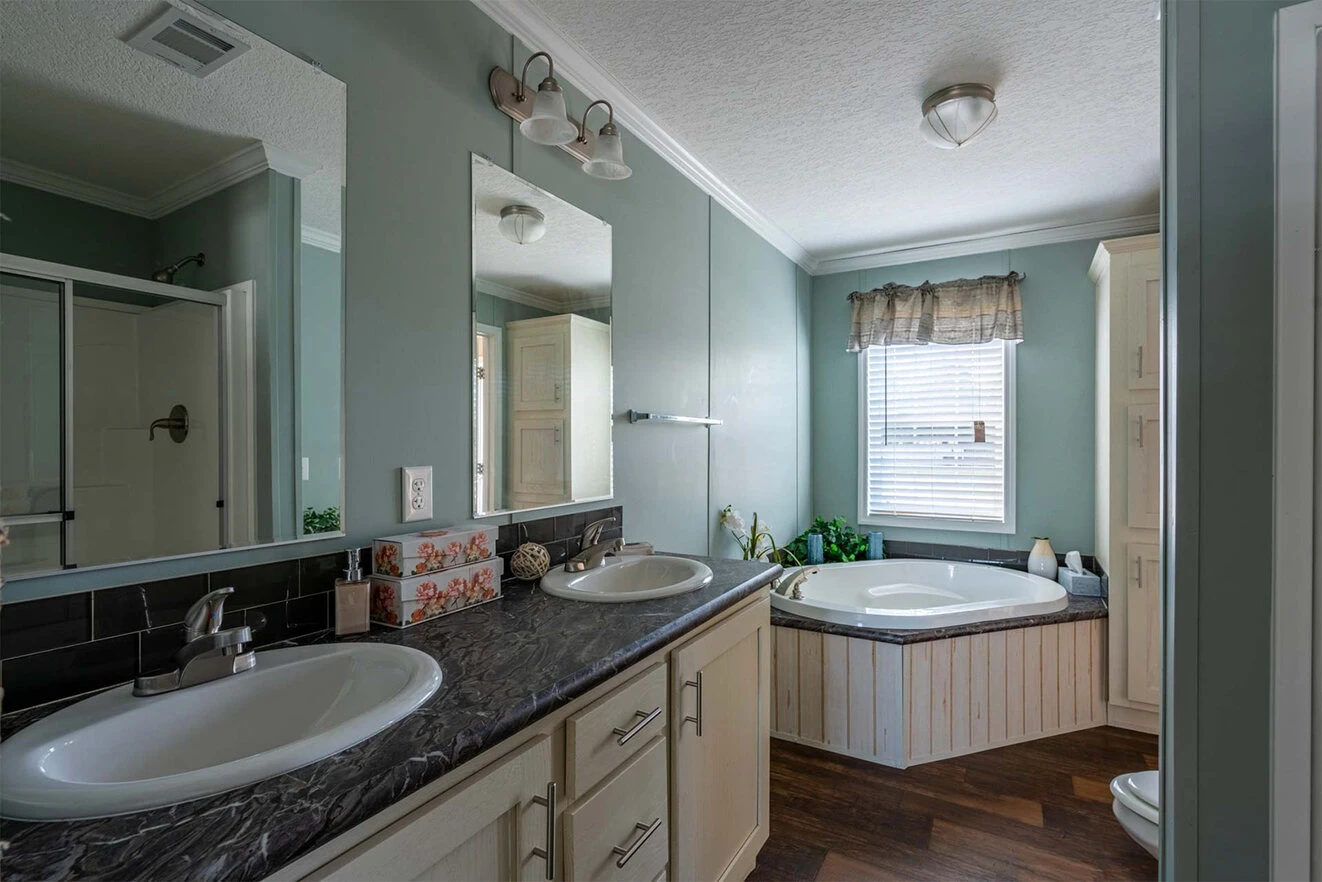 te28523c_17_1713813627837_1323_12 Bathroom with double sinks, a black marble countertop, a corner bathtub under a window with a valance, and a glass-enclosed shower reflected in the mirror.