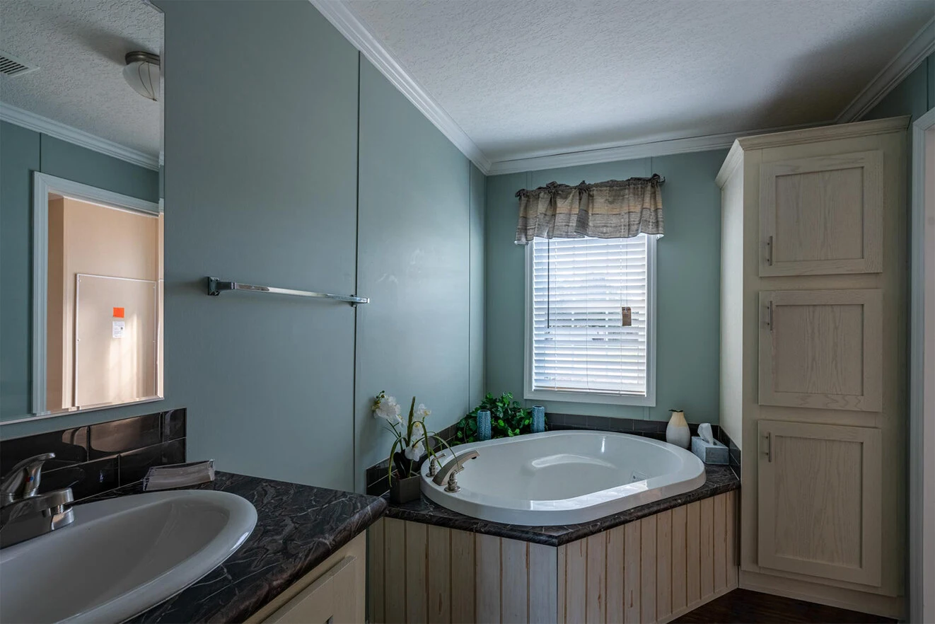te28523c_2_1713813699884_1323_12 A bathroom with a round bathtub beneath a window, a sink with a marble countertop, light blue walls, and a tall storage cabinet.