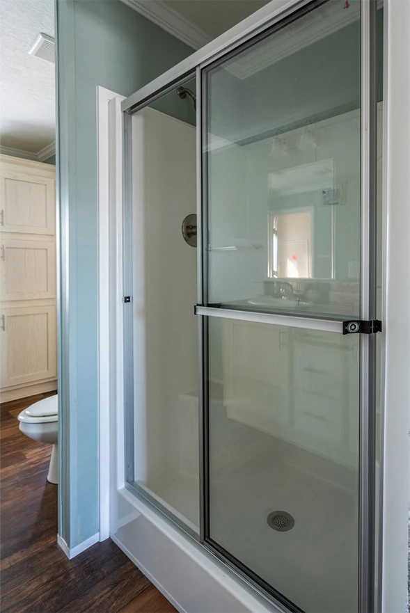 te28523c_3_1713813696525_589_12 A glass shower stall with a sliding door in a bathroom with wood flooring and light-colored cabinetry.