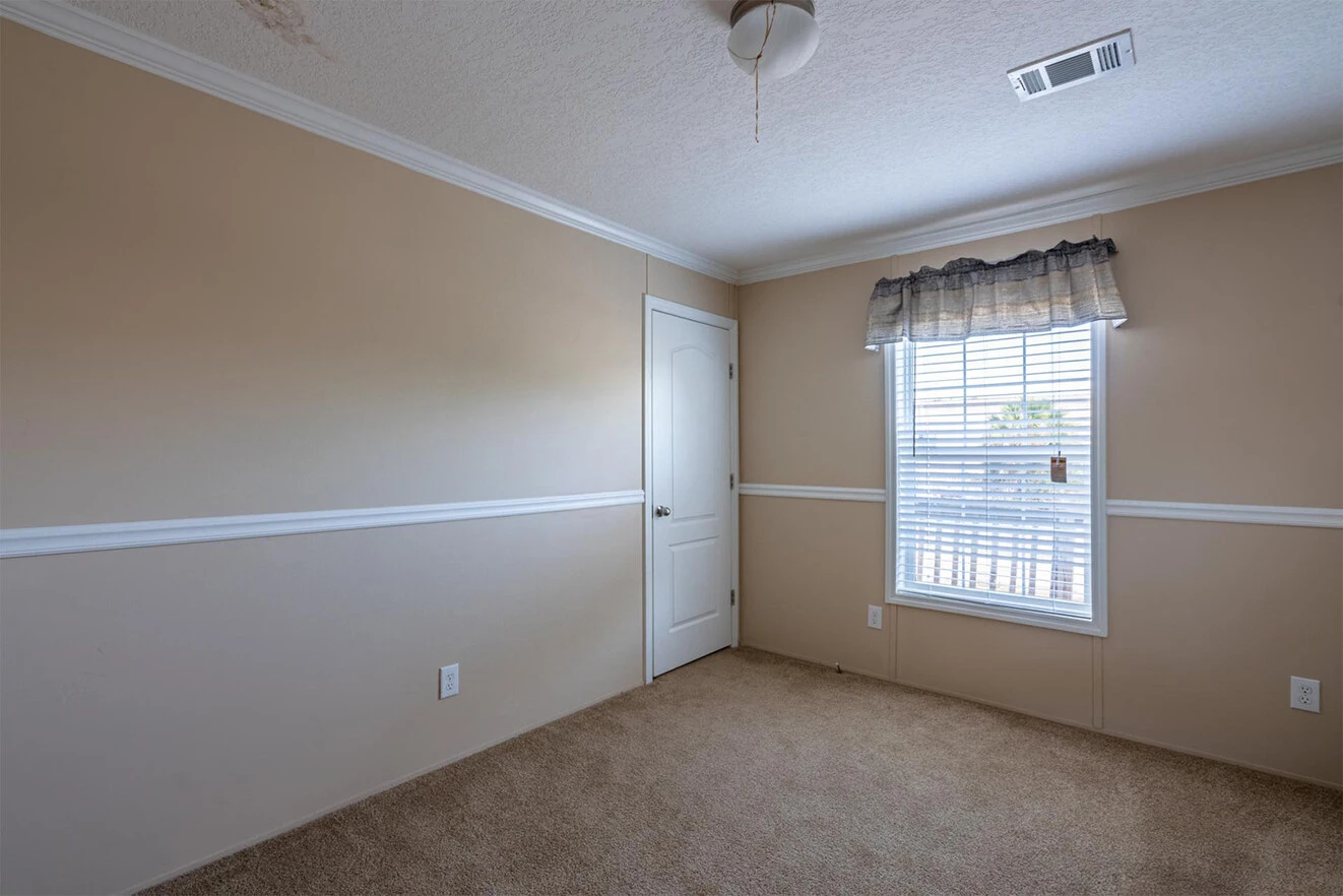 te28523c_6_1713813685784_1323_12 Empty beige room with carpeted floor, a single window with a valance, white door, ceiling fan, and visible electrical outlets on the walls.