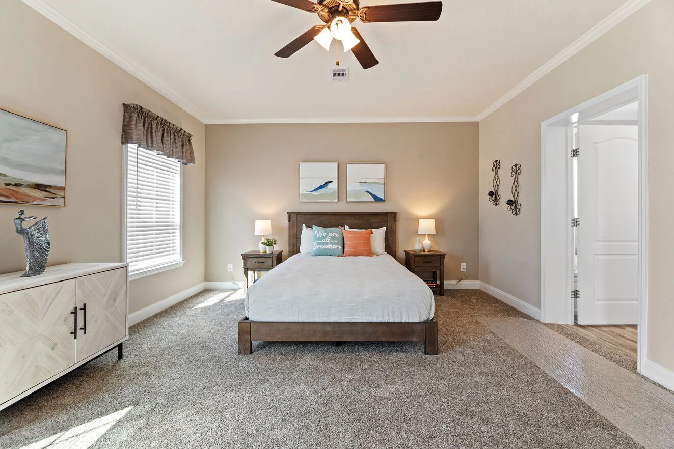 A neatly arranged bedroom with a double bed, two nightstands with lamps, a ceiling fan, carpeted floor, and natural light from a window.