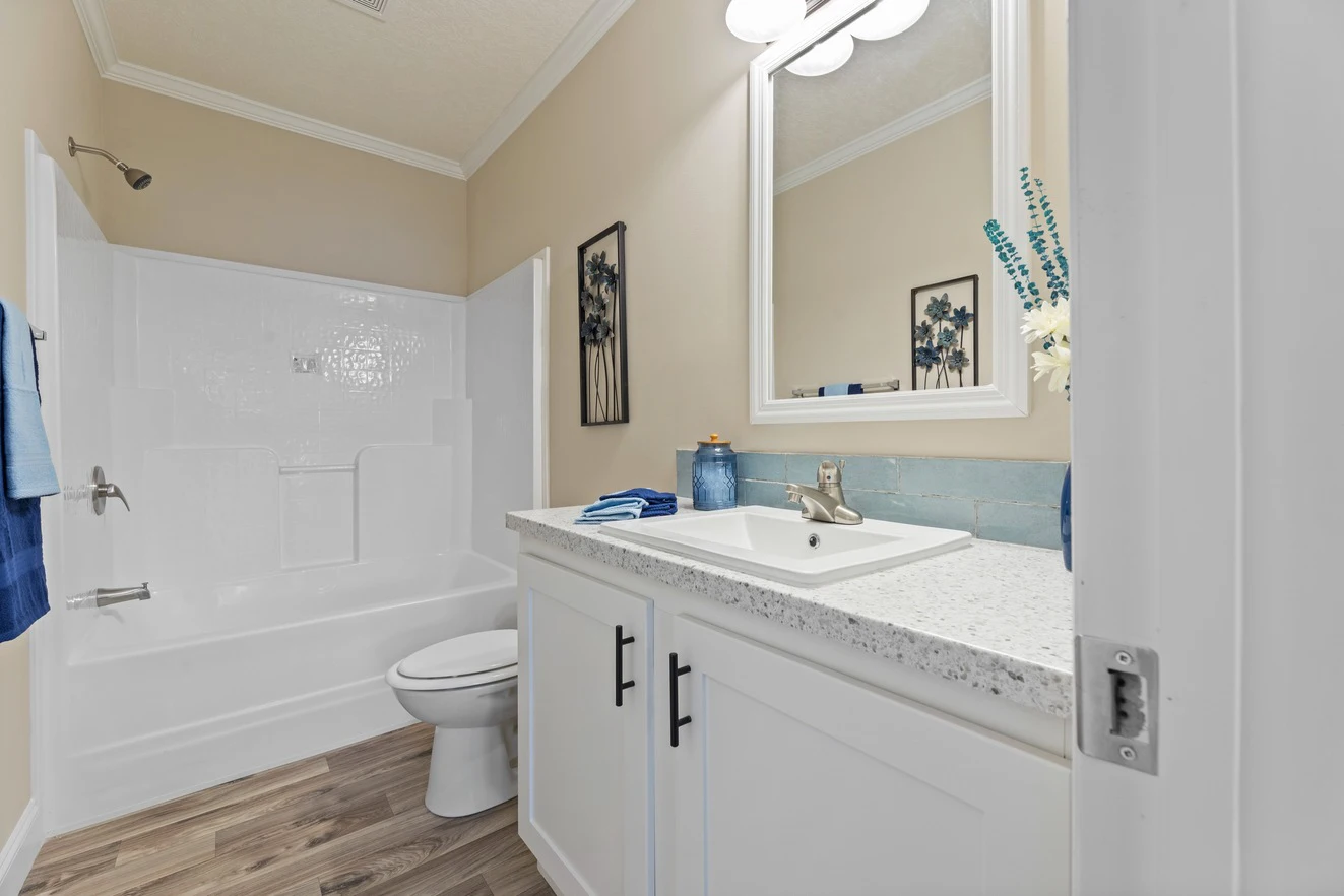 Modern bathroom with white cabinets, a sink, a toilet, a bathtub-shower combo, wood-patterned floor, and neutral walls decorated with framed art and blue accents.