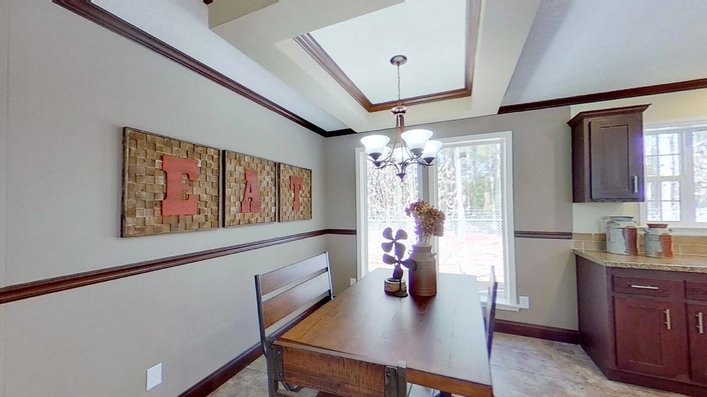 A dining area with a wooden table and chairs, a modern chandelier, wall art spelling "EAT," and sunlight coming through a window next to dark wood kitchen cabinets.