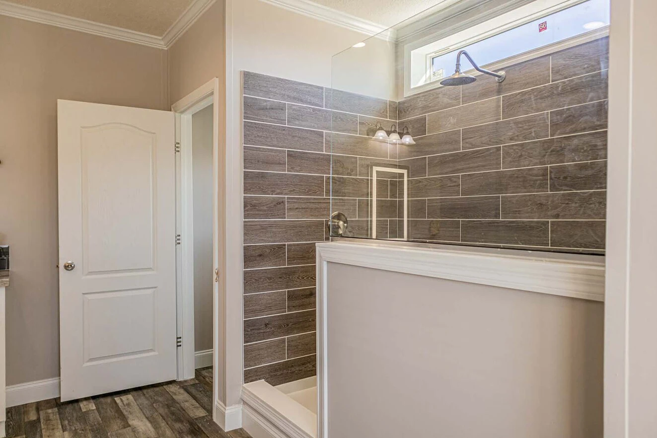 Modern bathroom with a walk-in shower featuring gray wood-look tiles, a glass partition, and a small window above the shower area.