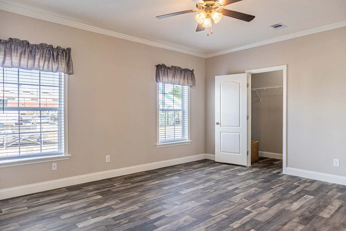 Empty room with two windows, gray wood-style flooring, beige walls, ceiling fan with lights, and an open door leading to a walk-in closet.