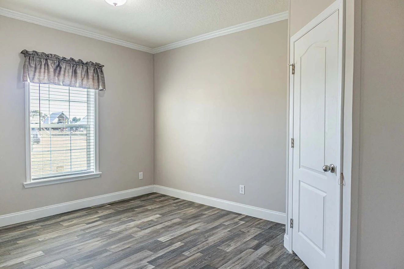 Empty room with light-colored walls, wood-patterned flooring, a window with blinds and valance, and a closed white door.