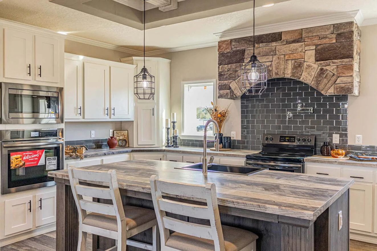 Modern kitchen with white cabinets, a stone range hood, black tile backsplash, stainless steel appliances, and a wooden island with seating for three.