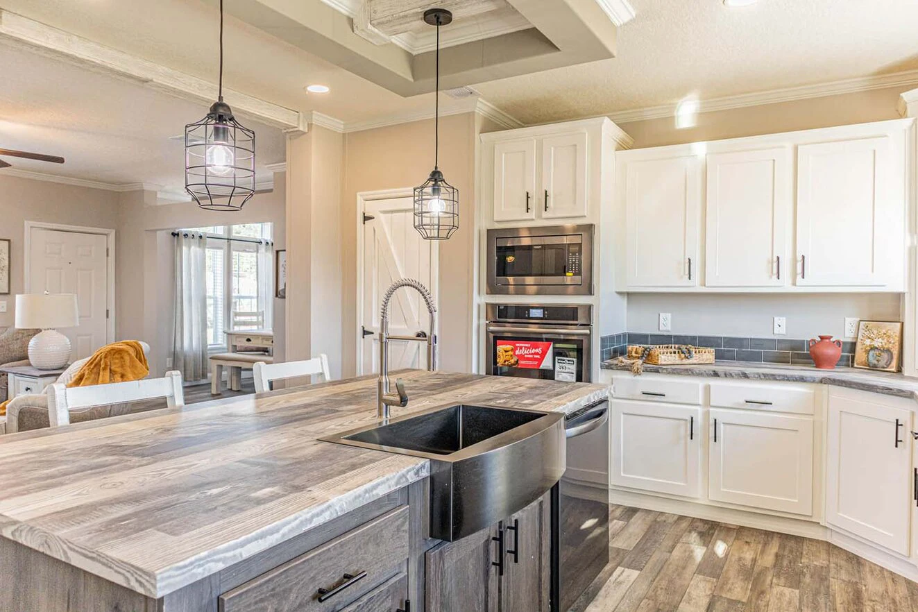 Modern kitchen with a farmhouse sink, wood island, pendant lights, white cabinets, built-in microwave, and stainless steel appliances.