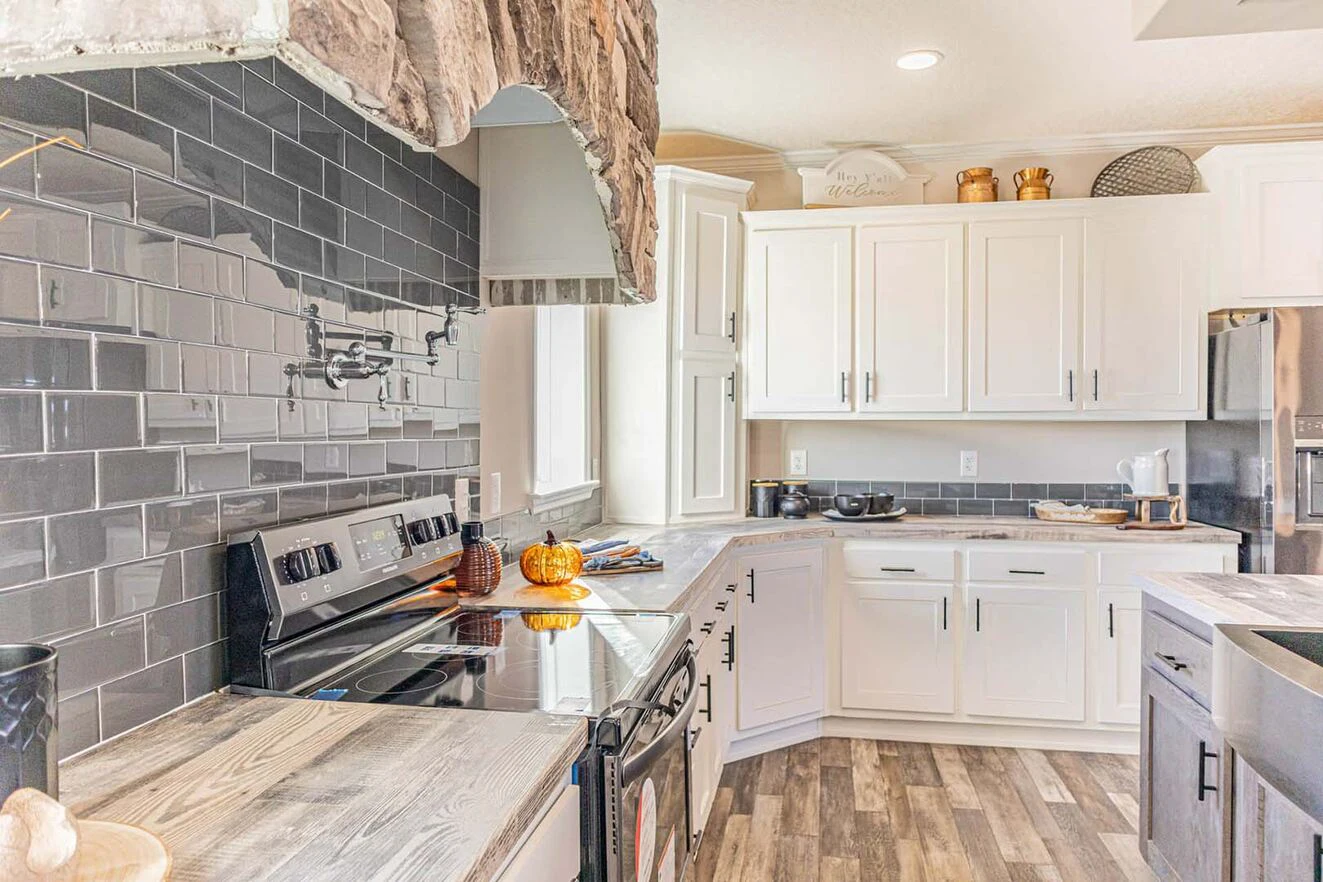 Modern kitchen with white cabinets, gray subway tile backsplash, stainless steel appliances, and wooden countertops; small pumpkins sit on the stove.