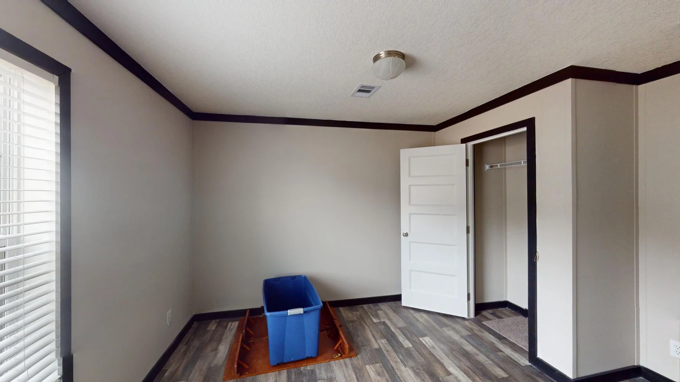 Empty room with gray walls and wood-patterned flooring, featuring an open closet and door, a blue plastic bin, and a window with blinds on the left.