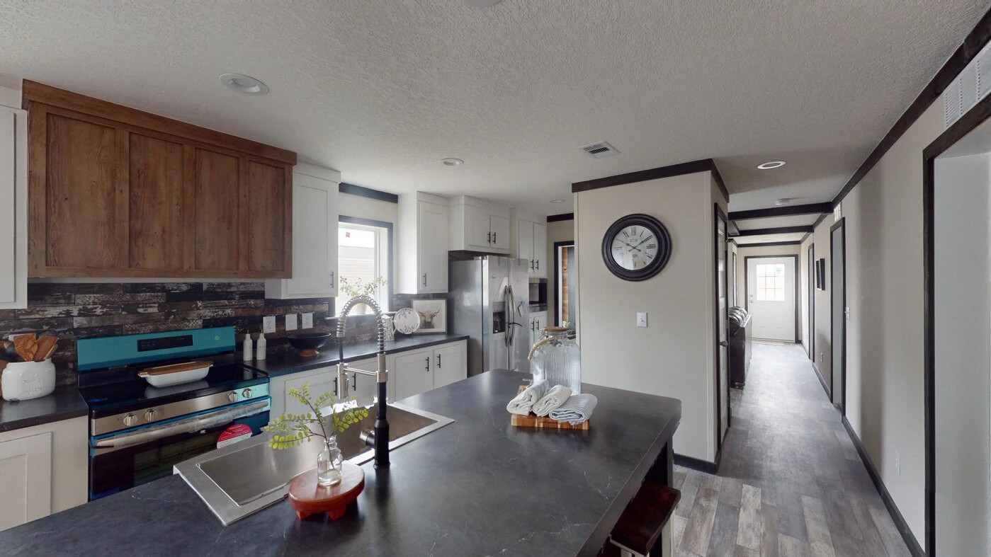 Modern kitchen with black countertops, white cabinets, stainless steel appliances, a wall clock, and a view of a hallway leading to another room.