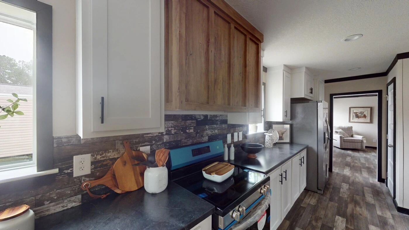 Modern kitchen with white cabinets, wood accents, black countertops, stainless steel appliances, and a visible living area in the background.