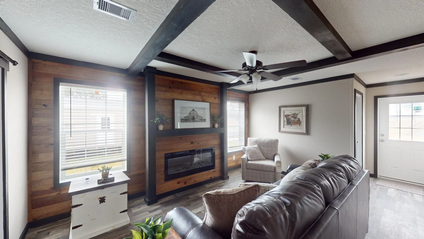 A living room with wood accents, large windows, a ceiling fan, a fireplace, armchairs, a sofa, and a door leading outside.