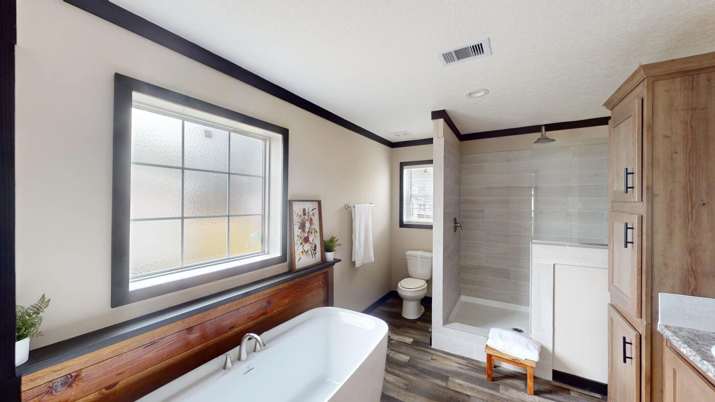 Modern bathroom with a freestanding tub, walk-in shower, toilet, large frosted window, wooden cabinets, towel rack, and decorative artwork on the wall.