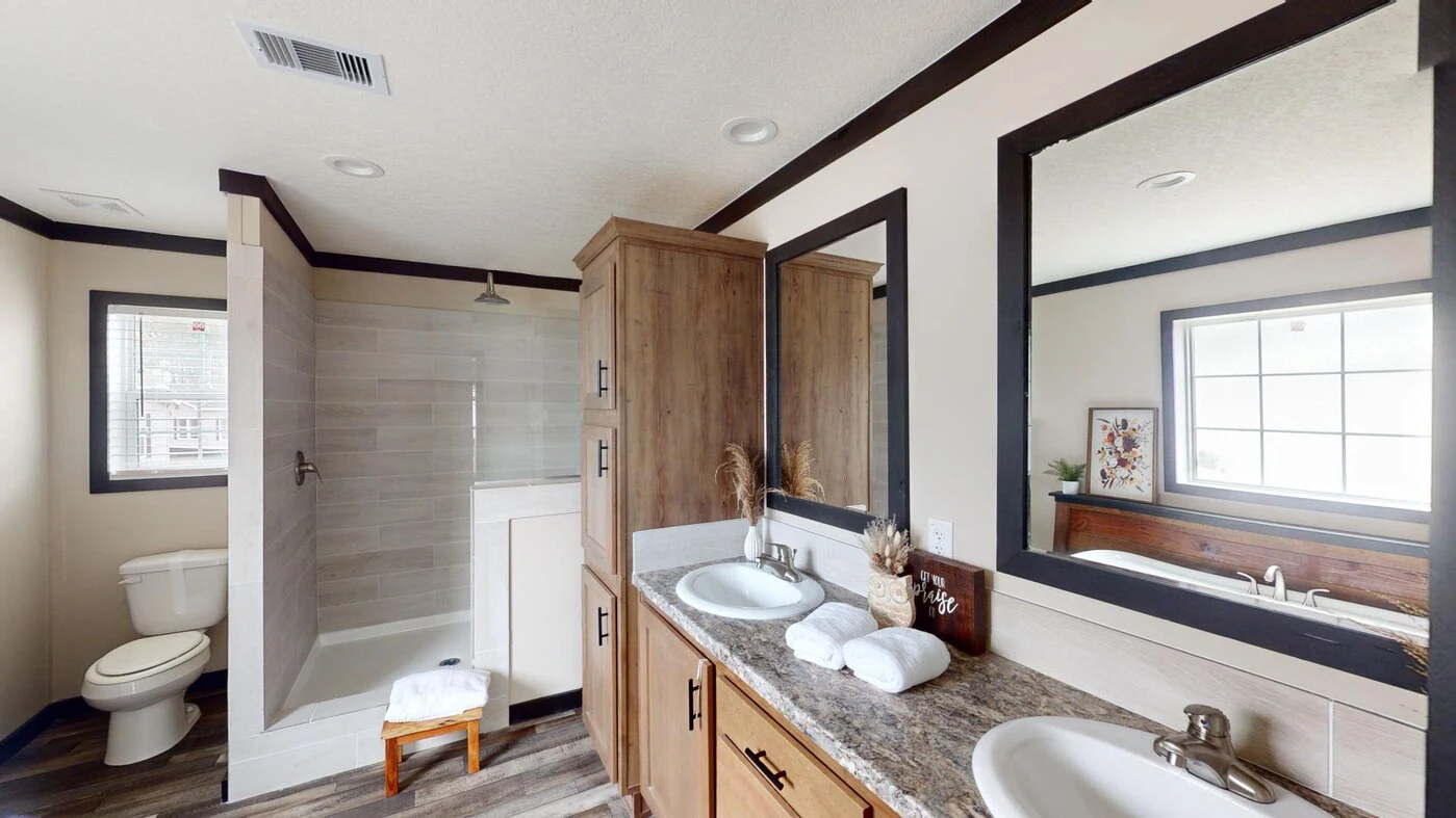 Modern bathroom with a walk-in shower, double sinks, wooden cabinets, large mirror, toilet, and a bathtub by a window. Towels and decorative items are on the countertop.