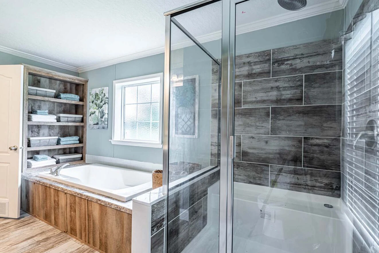 Modern bathroom with glass shower, built-in bathtub, tiled walls, open shelving with towels, large window, and gray-blue painted walls.
