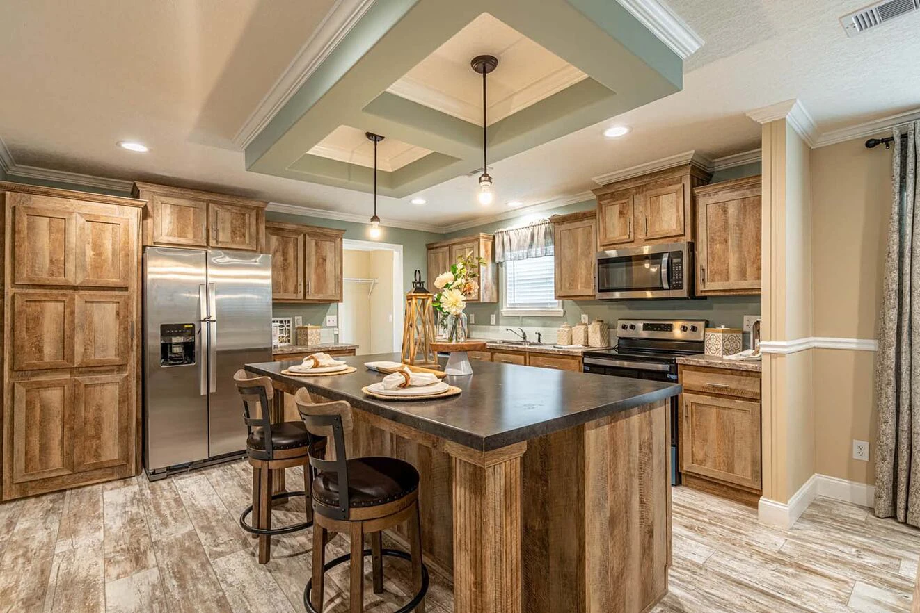 Modern kitchen with wood cabinets, center island with two stools, stainless steel appliances, pendant lights, and tile flooring. Table set for two with flowers on the island.