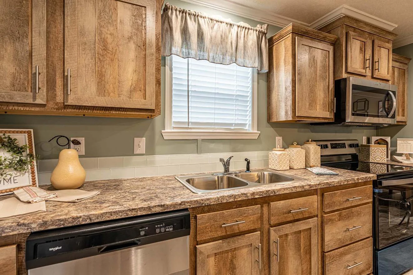 A kitchen with wood cabinets, a double sink, stainless steel dishwasher, stove, microwave, and a window with blinds and a valance above the sink.