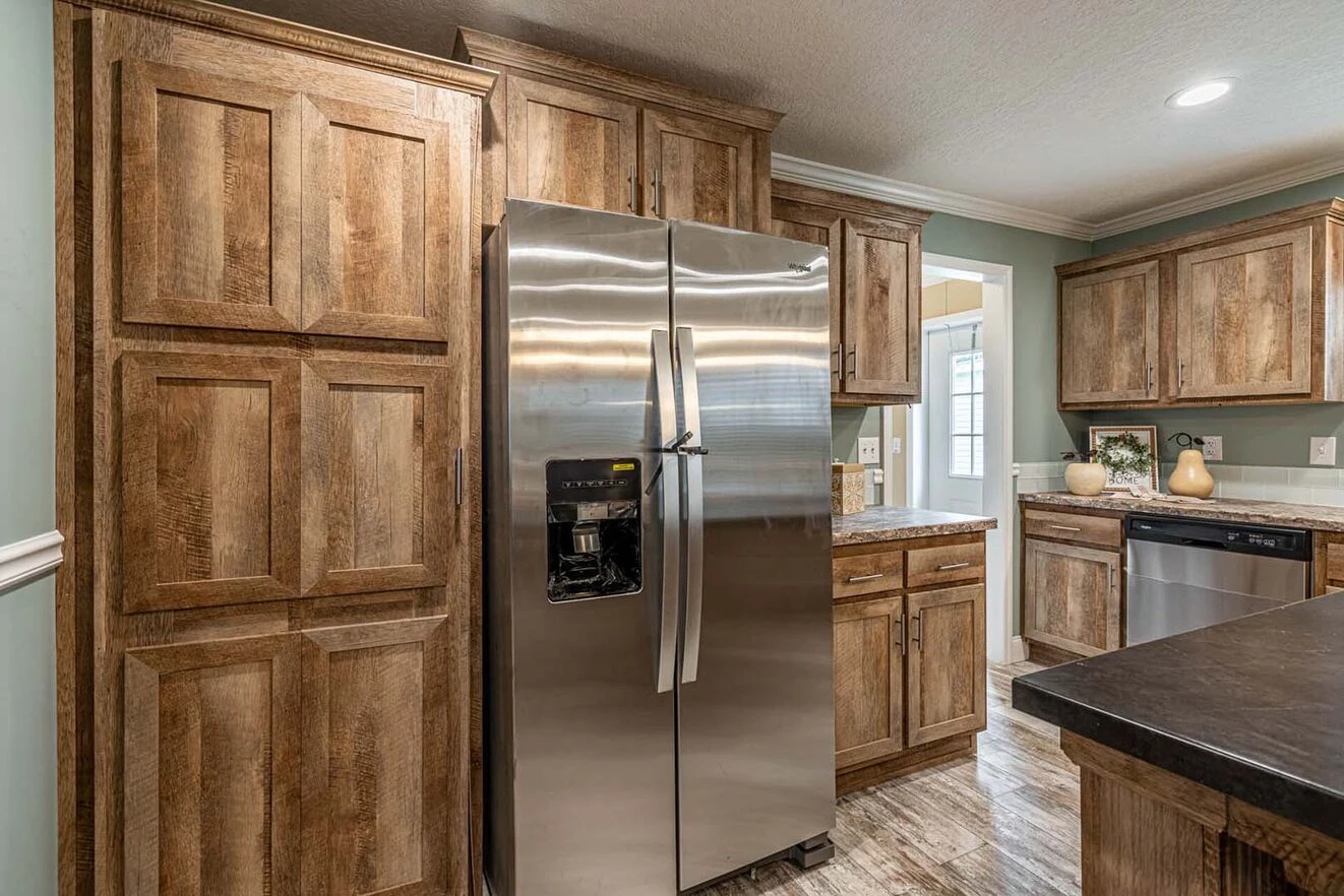 A modern kitchen with wooden cabinets, a stainless steel refrigerator, a dishwasher, and a countertop under bright indoor lighting.