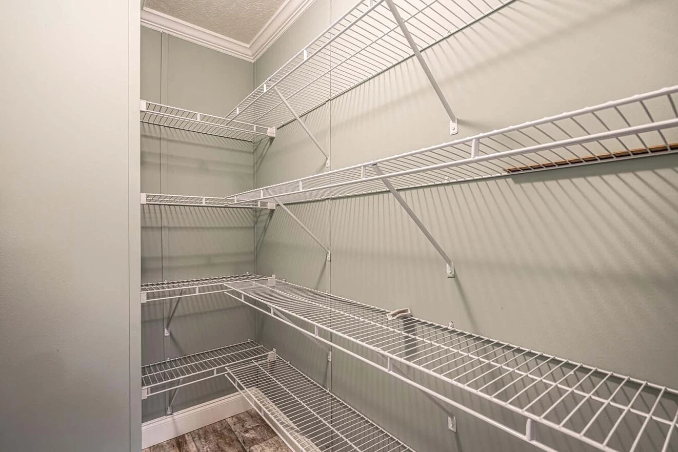 Empty walk-in pantry with multiple rows of white wire shelves against light gray walls and wood-patterned flooring.