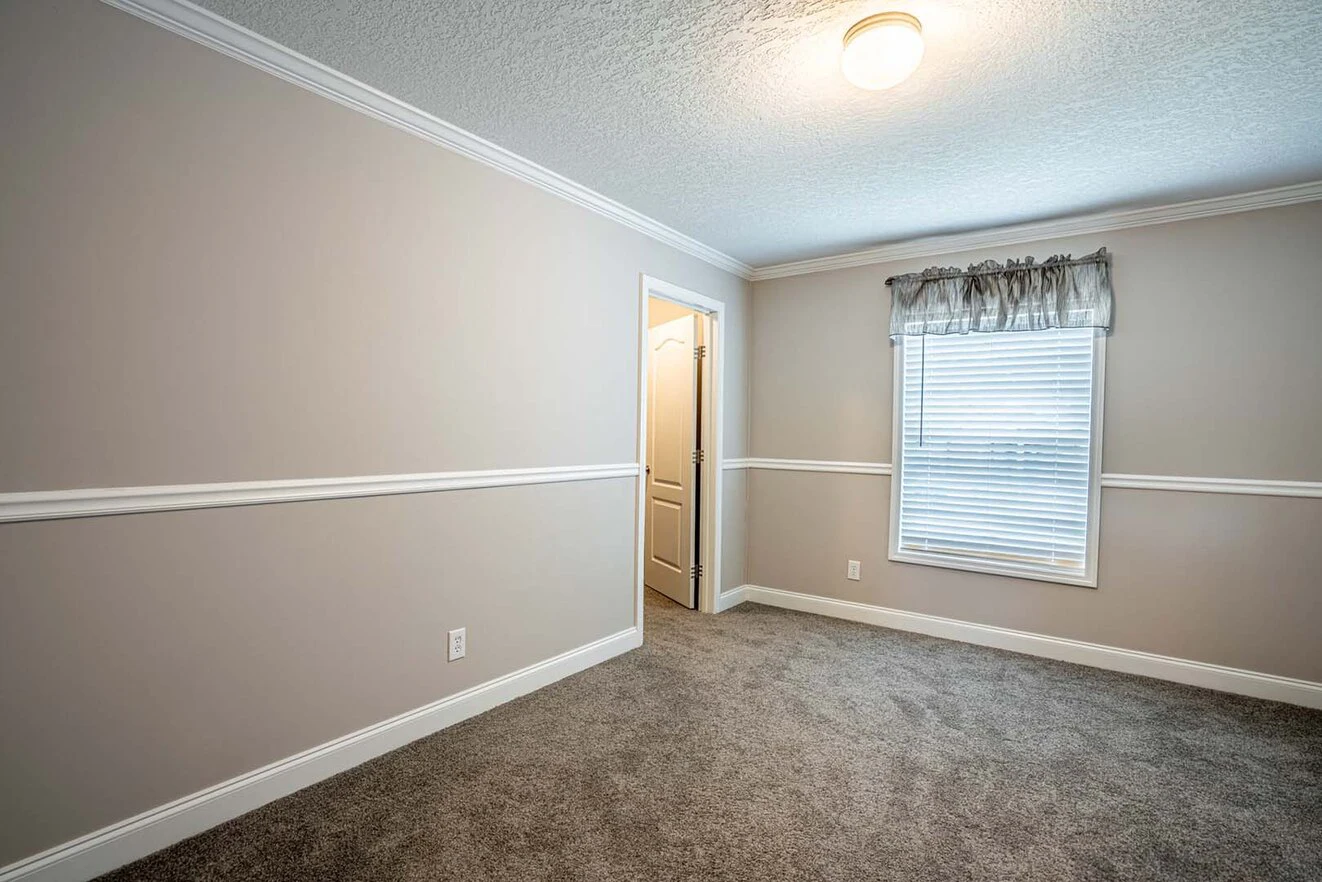 Empty room with beige walls, white trim, carpeted floor, a window with blinds and valance, and an open door leading to another area. Ceiling light is on.