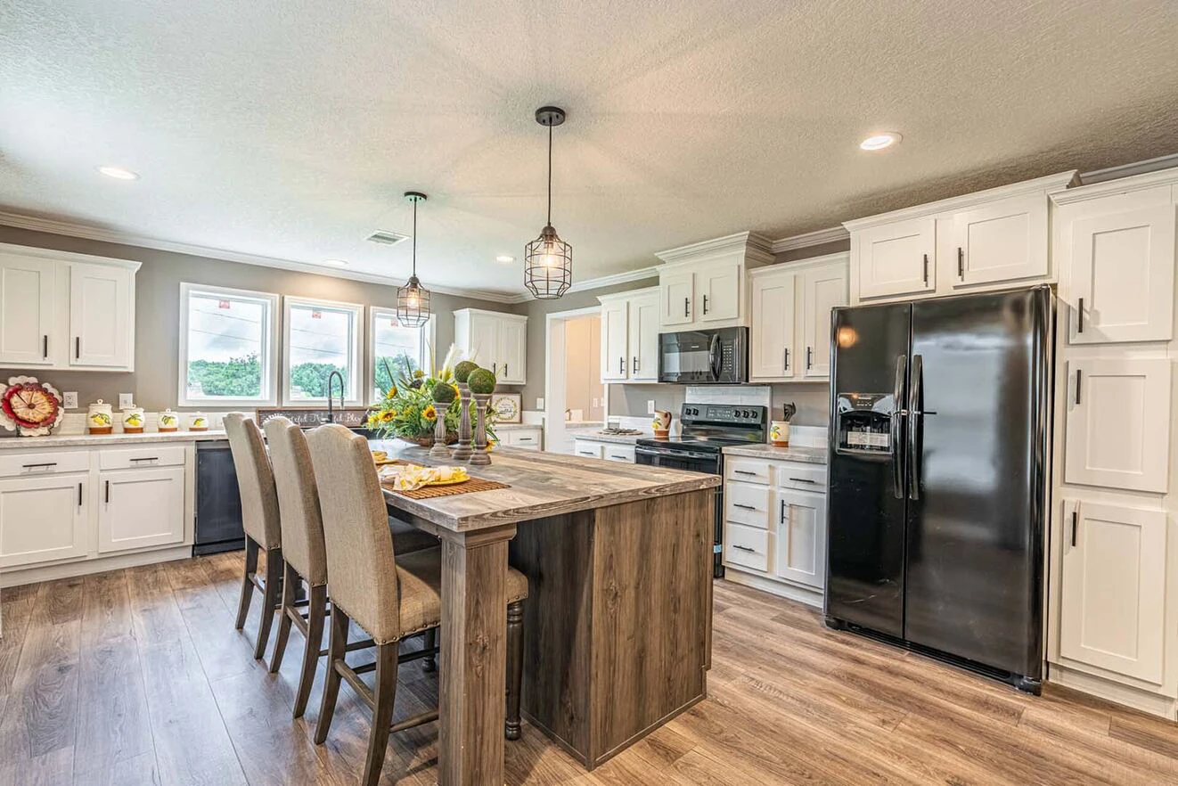 Modern kitchen with white cabinets, black appliances, a large wooden island with seating for four, pendant lights, and wood flooring.
