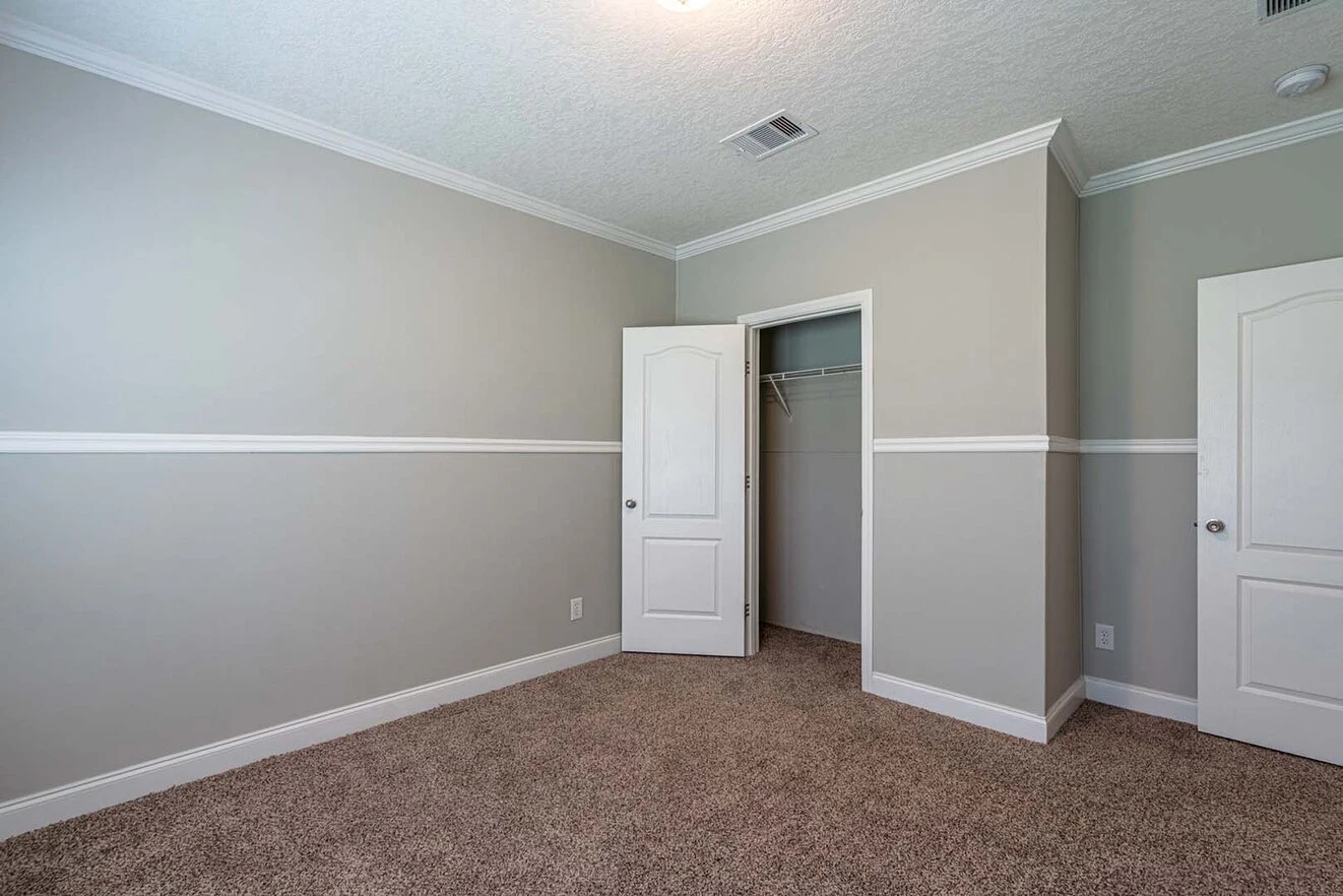 Empty room with light gray walls, white trim, beige carpet, an open closet door, and another closed door. Ceiling vent and light visible.