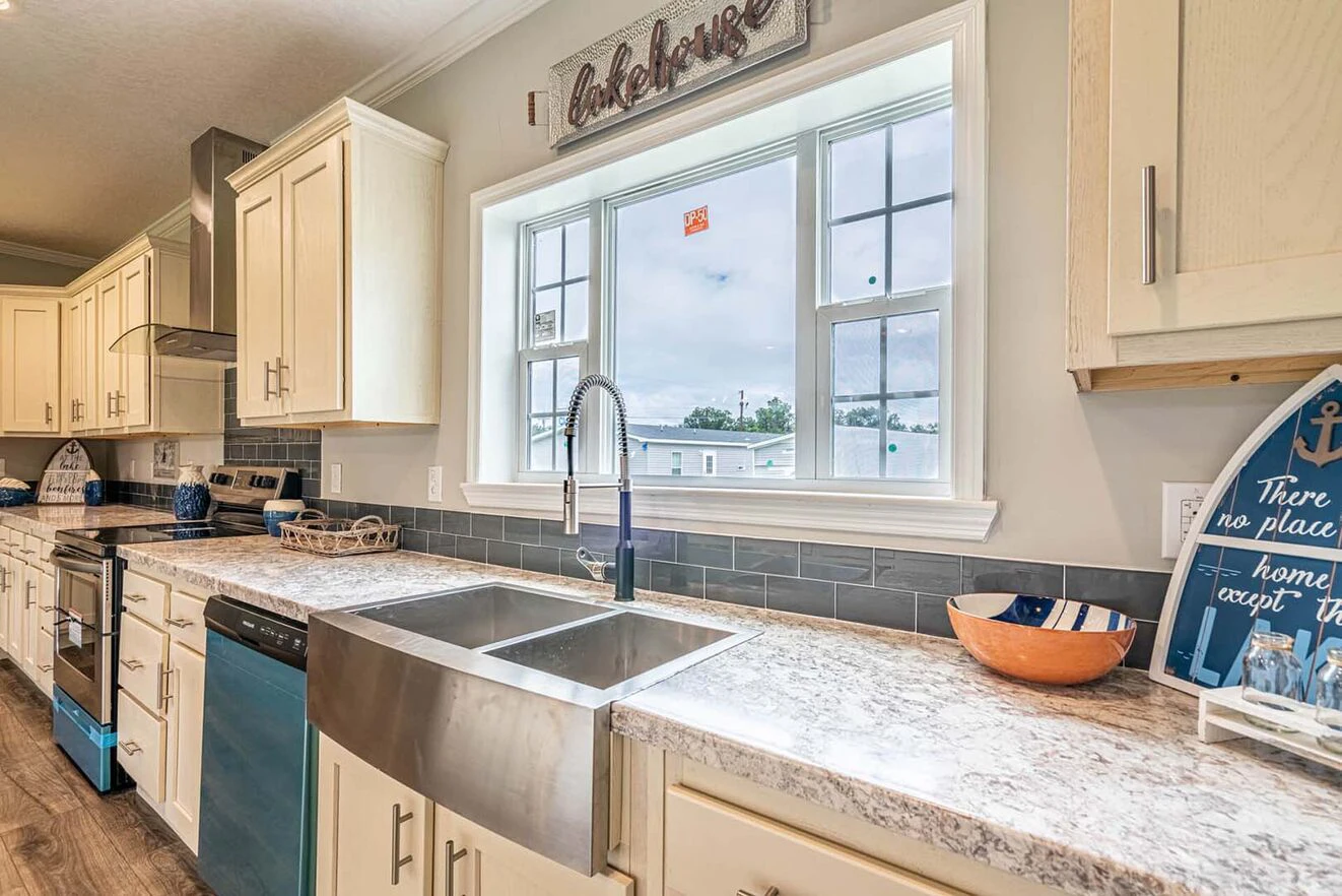 Modern kitchen with white cabinets, stainless steel farmhouse sink, marble countertop, and a large window above the sink letting in natural light.