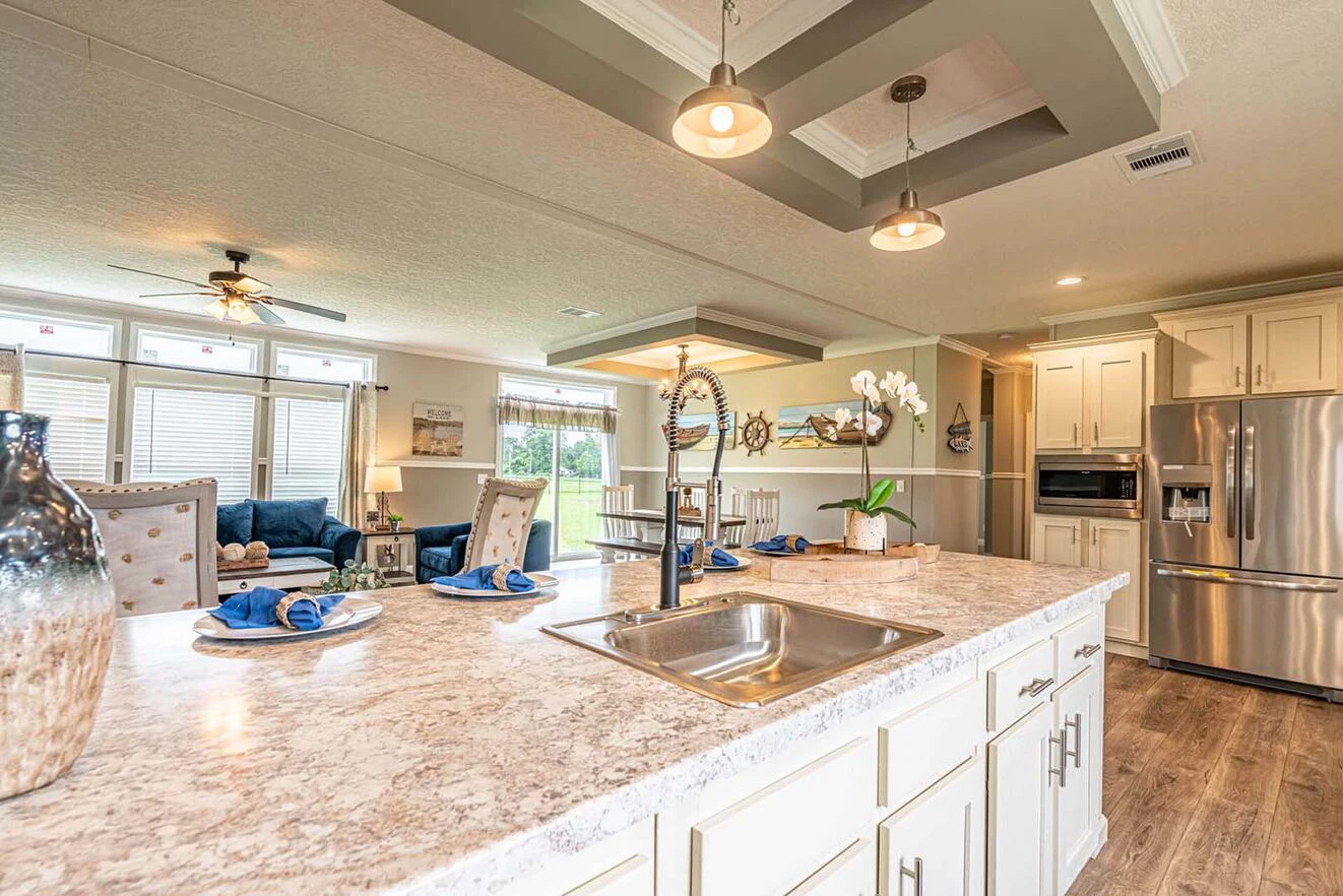 Modern kitchen with marble countertop island, stainless steel appliances, hanging lights, and open view to a furnished living room with large windows.