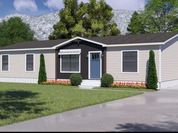 A single-story beige manufactured home with a blue front door, white trim, and simple landscaping, set against trees and a mountain backdrop.