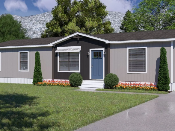 A gray, single-story manufactured home with a blue front door, small front porch, two shrubs, and flower beds, set on a lawn with trees and a mountain in the background.