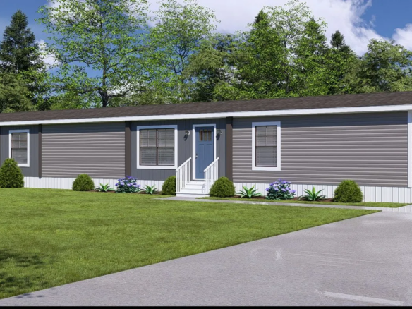 A single-story, gray manufactured home with white trim sits on a green lawn, featuring a small front porch, shrubs, and a paved driveway under a partly cloudy sky.