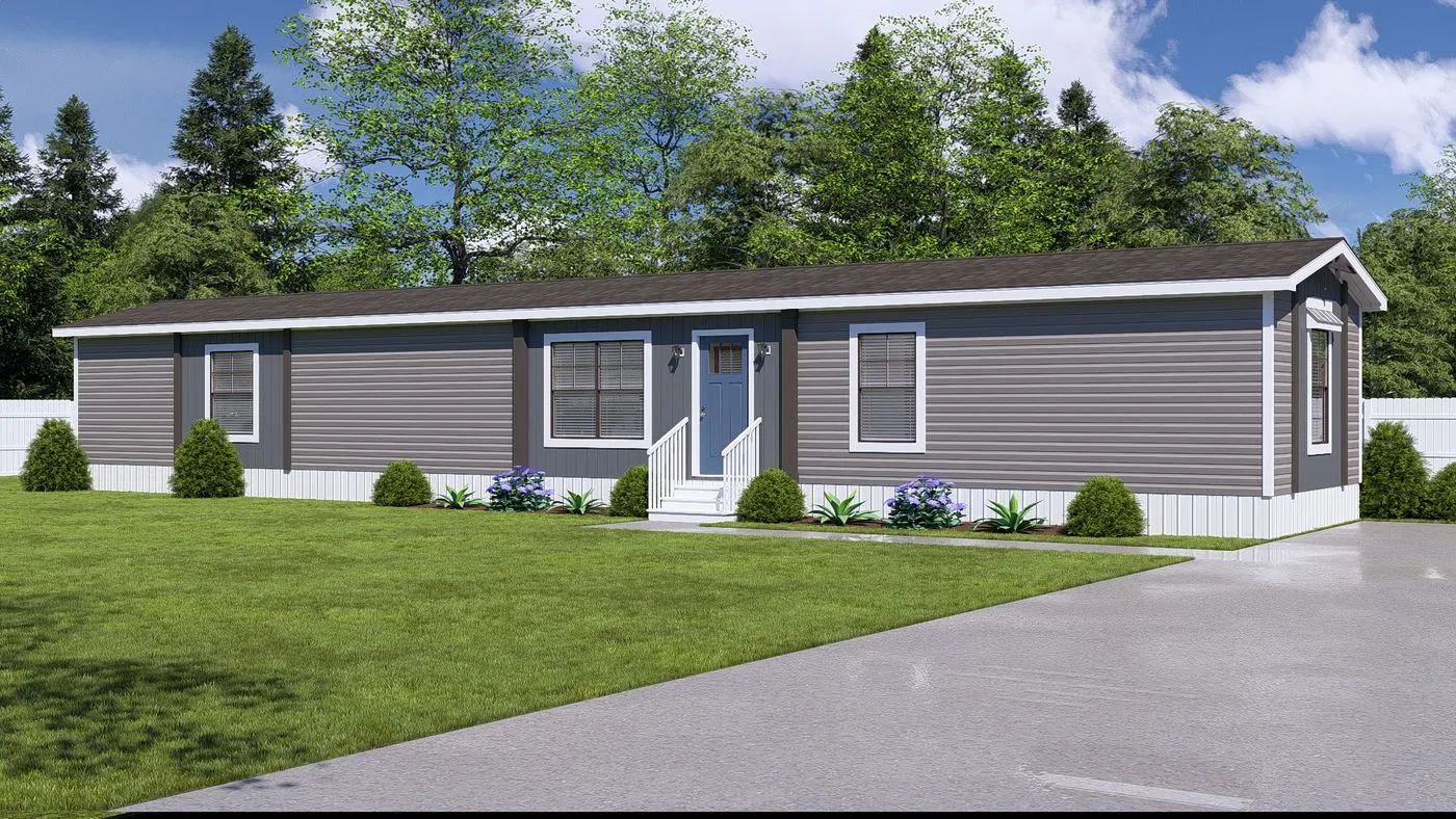 A single-story, gray manufactured home with white trim sits on a green lawn, featuring a small front porch, shrubs, and a paved driveway under a partly cloudy sky.