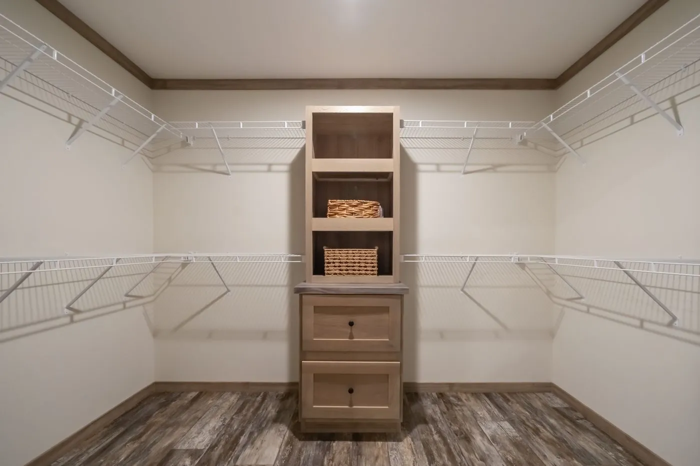 Empty walk-in closet with wire shelving around three walls, a wooden shelving unit with drawers, and baskets on display; wood-patterned floor.