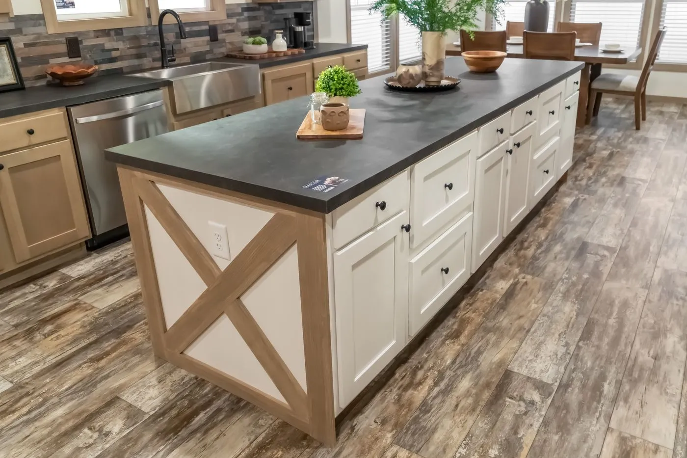 A kitchen island with white cabinets, a black countertop, and a wood accent on the side, situated on a wood-patterned floor in a modern kitchen.