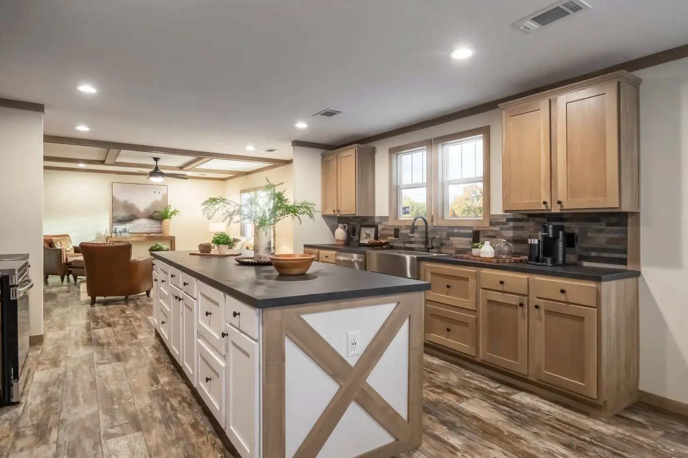 Modern kitchen with wood cabinets, center island, stainless steel appliances, farmhouse decor, and open layout leading to a living area with brown furniture.