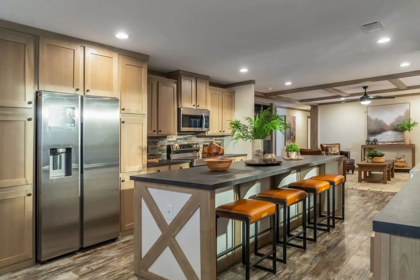 Modern kitchen with wood cabinets, stainless steel appliances, a center island with three orange bar stools, and potted plants as decor. Dining and living areas are visible in the background.