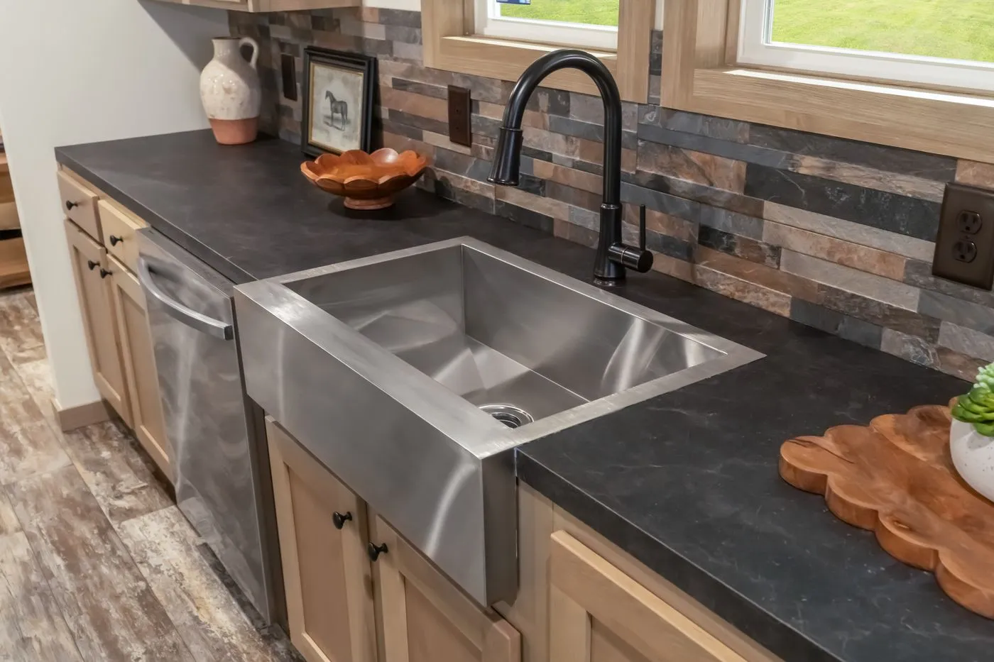 Modern kitchen countertop with a stainless steel farmhouse sink, black faucet, decorative items, and a stone tile backsplash.