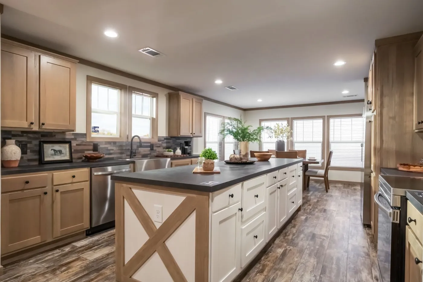 Spacious kitchen with wood cabinets, large island, stainless steel appliances, farmhouse sink, and a dining area with large windows and wood flooring.